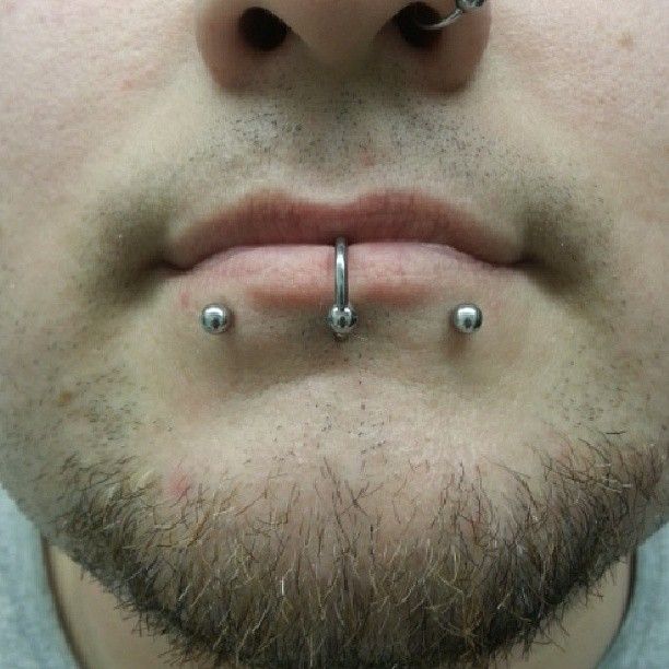 A close up of a man 's face with a beard and piercings.