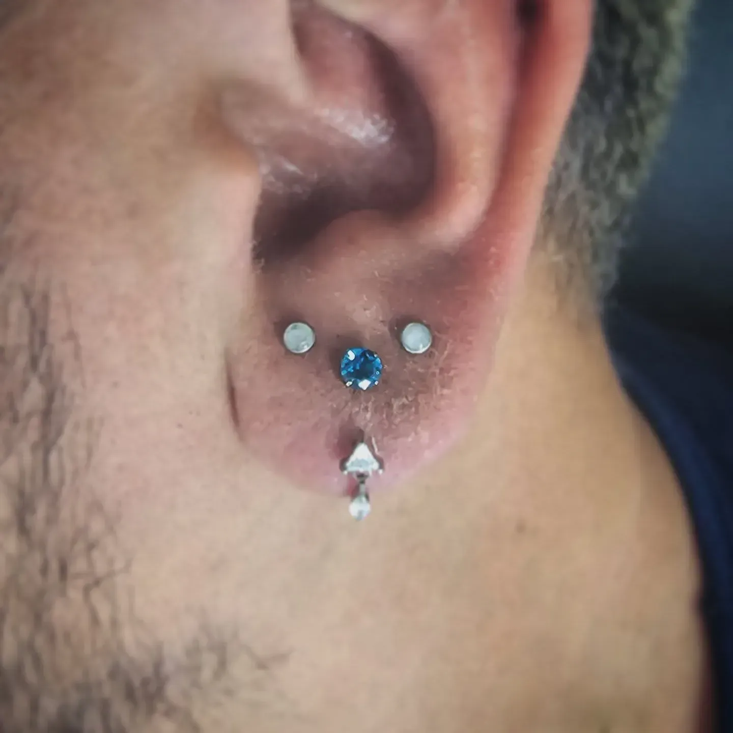A close up of a man 's ear with three piercings.
