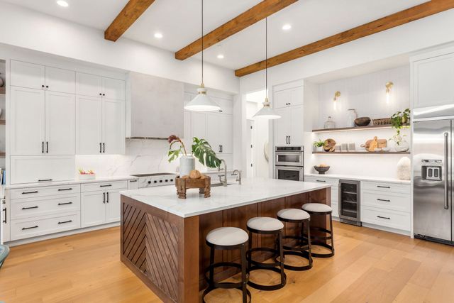 Bright white kitchen with island, bar stools, wood beams, and hardwood floors