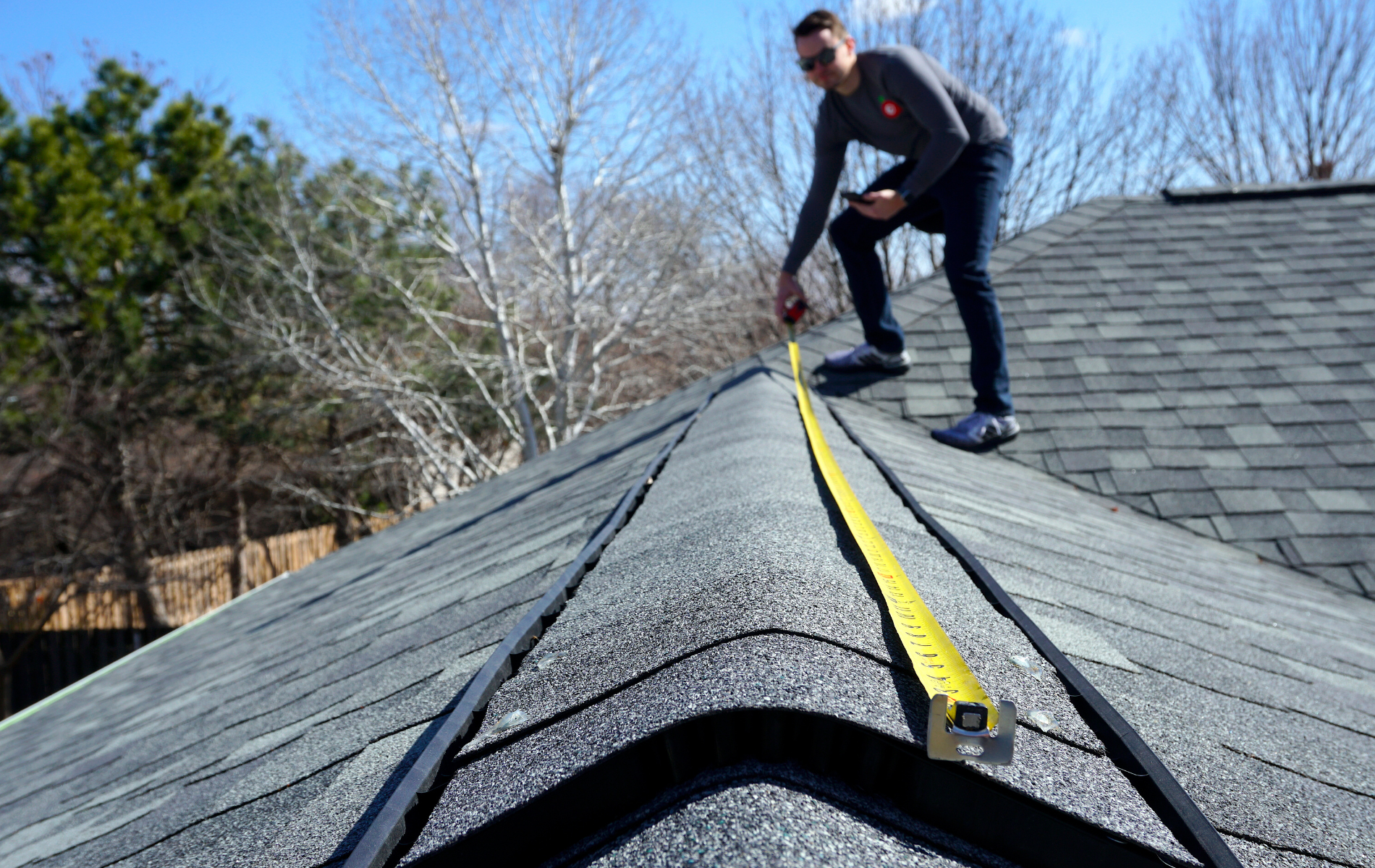 A man is measuring a roof with a tape measure.