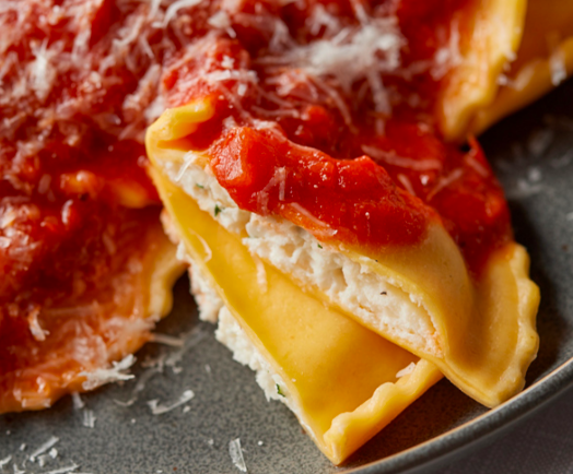 Close-up of cheese-filled ravioli topped with red tomato sauce and grated parmesan cheese on a plate.
