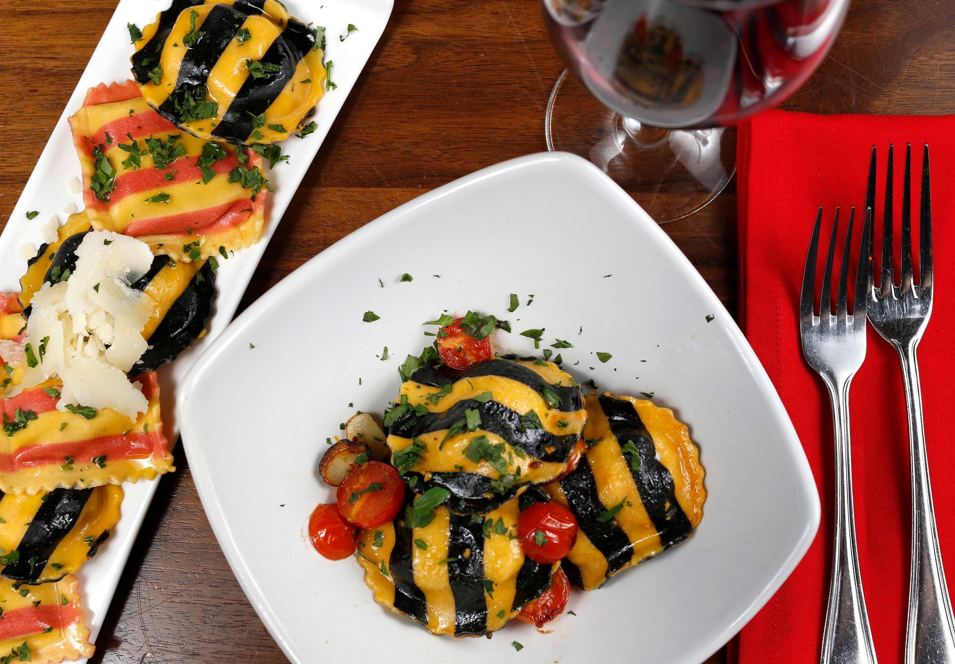 Striped black and yellow ravioli served on two white plates with cherry tomatoes and a glass of wine on a wooden table.