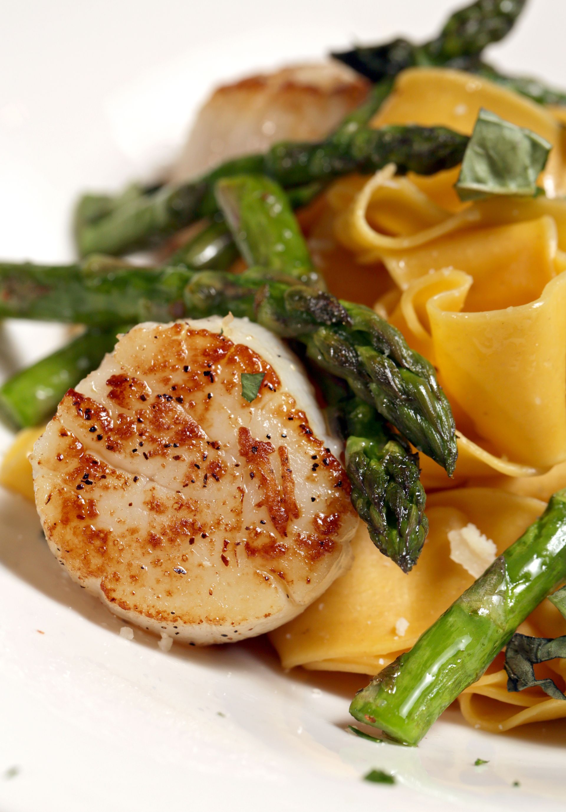 Seared scallops served with bright green asparagus spears and wide, golden pappardelle pasta.