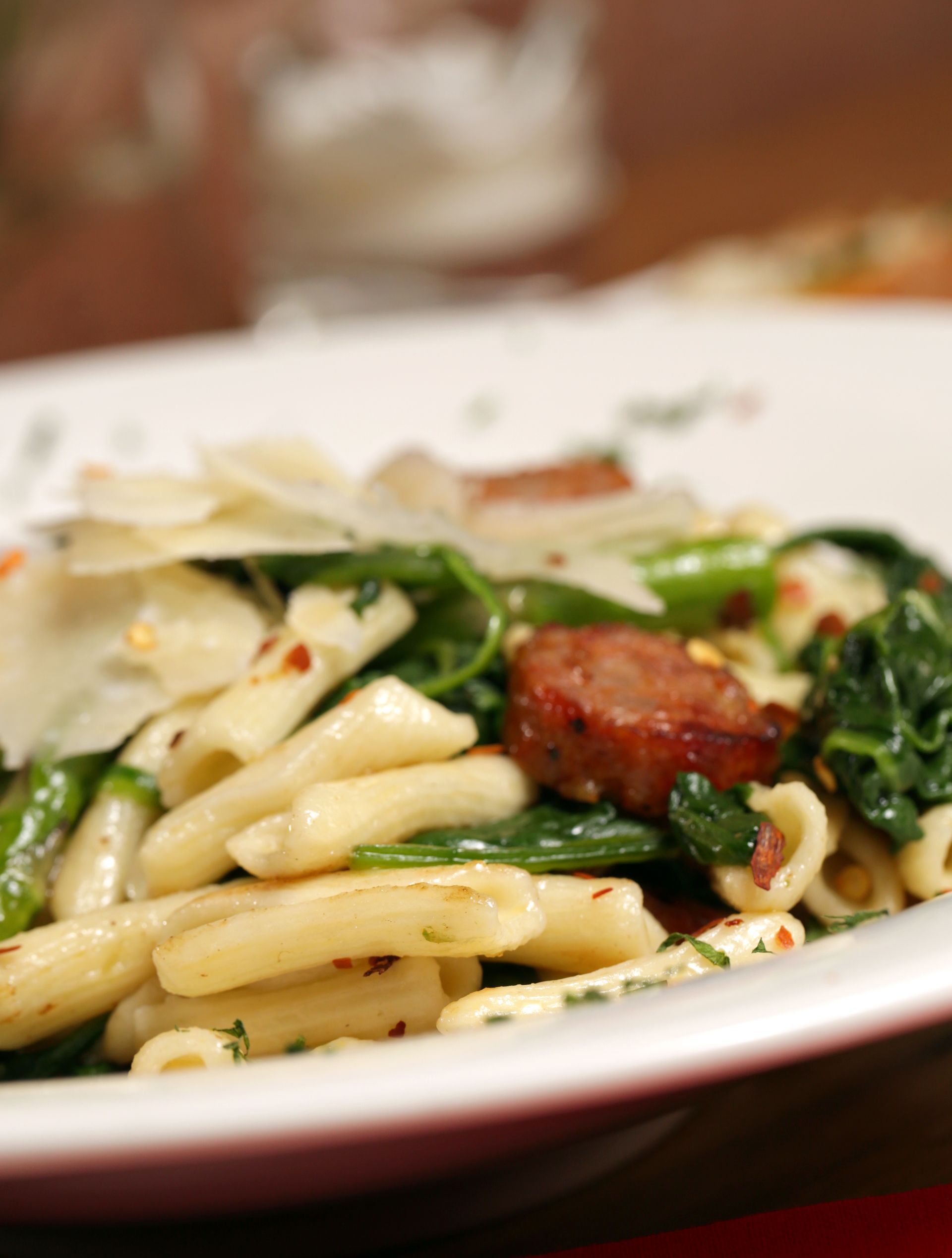 A plate of pasta tossed with sausage, spinach, and red pepper flakes, topped with shaved parmesan cheese.
