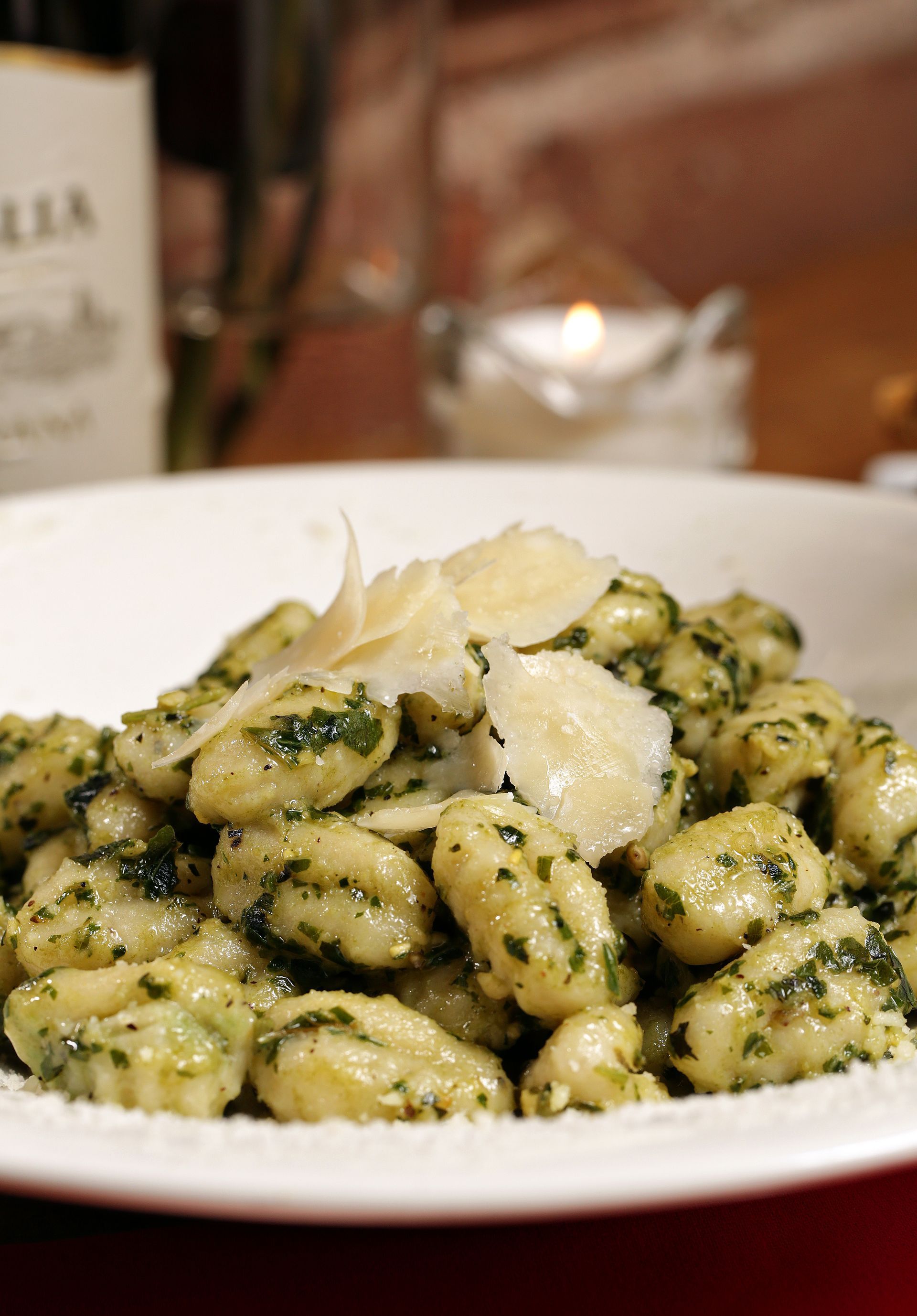 A plate of potato gnocchi coated in green pesto sauce and topped with thin shavings of Parmesan cheese.
