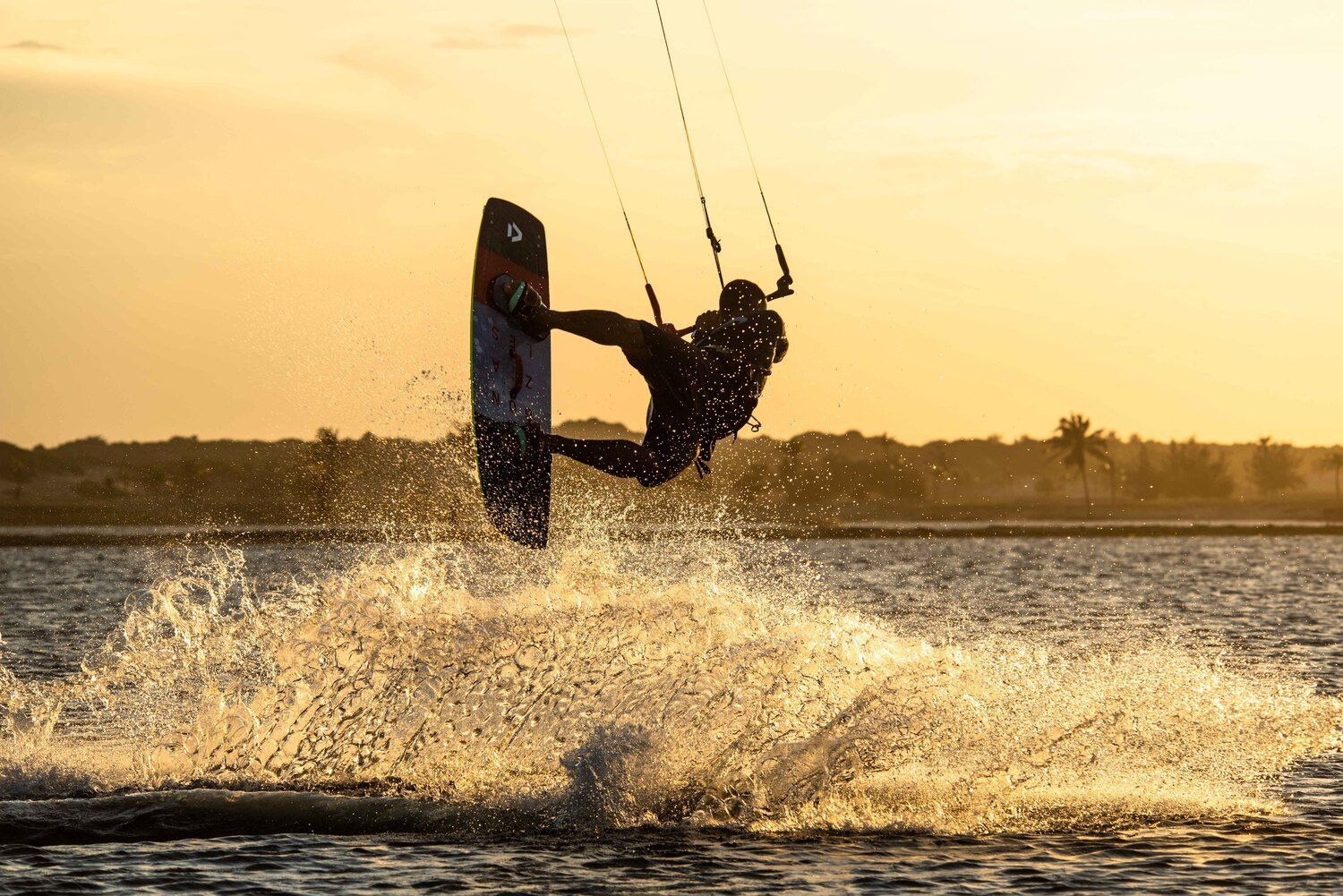 Uma pessoa está fazendo uma manobra em uma prancha de surfe na água ao pôr do sol.