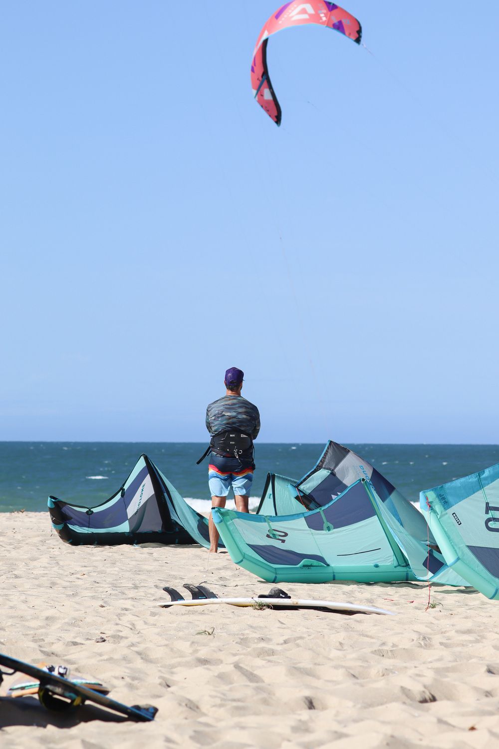 Um homem está de pé na praia olhando para uma pipa voando no céu.