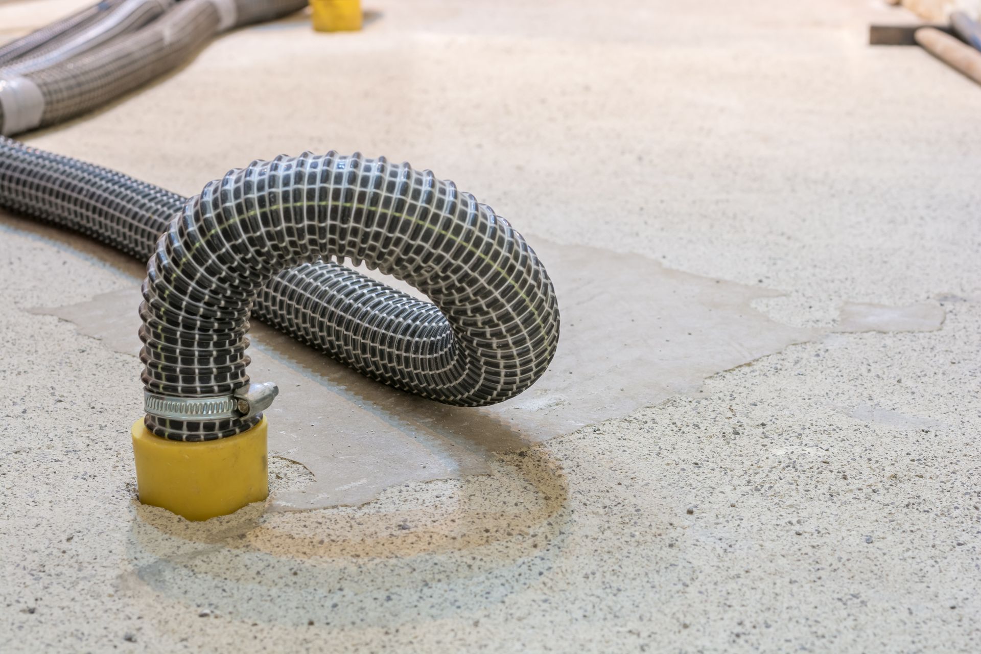 Flexibler grauer Schlauch mit gelben Anschlüssen auf einem hellen Betonboden.
