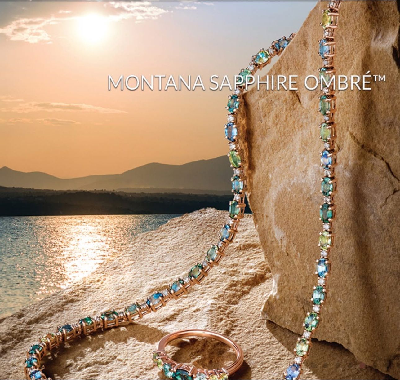 Montana sapphire ombre jewelry on a rock overlooking a lake with a sunset in the background.