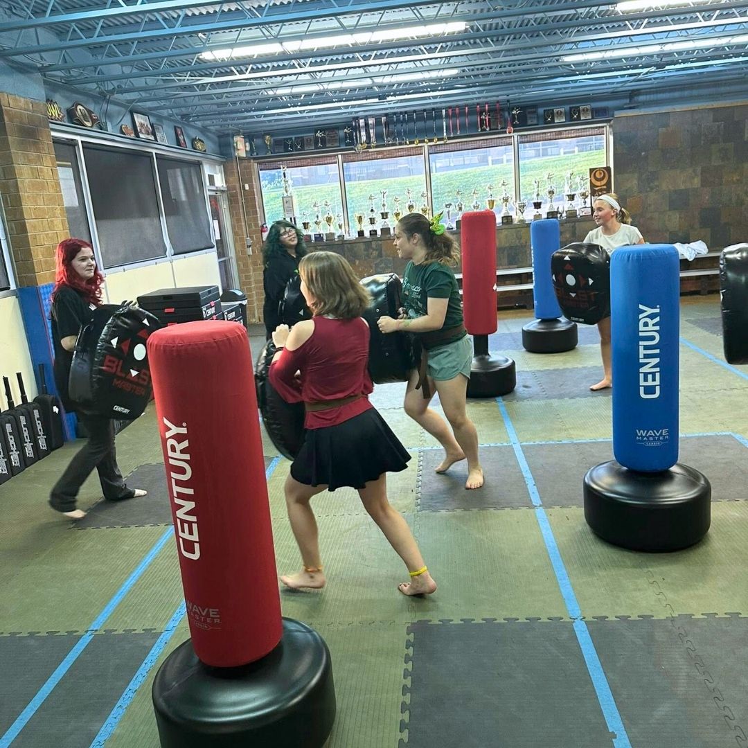 Two children in black and white martial arts uniforms practice a chokehold on a mat. One child smiles.