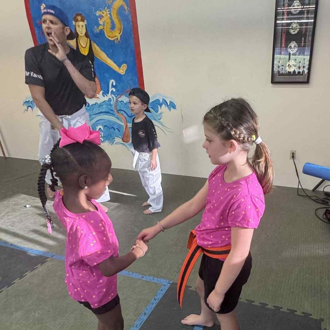 People practicing Brazilian Jiu-Jitsu. One person on the ground, another on top; two others grappling nearby. Black gis, indoor setting.