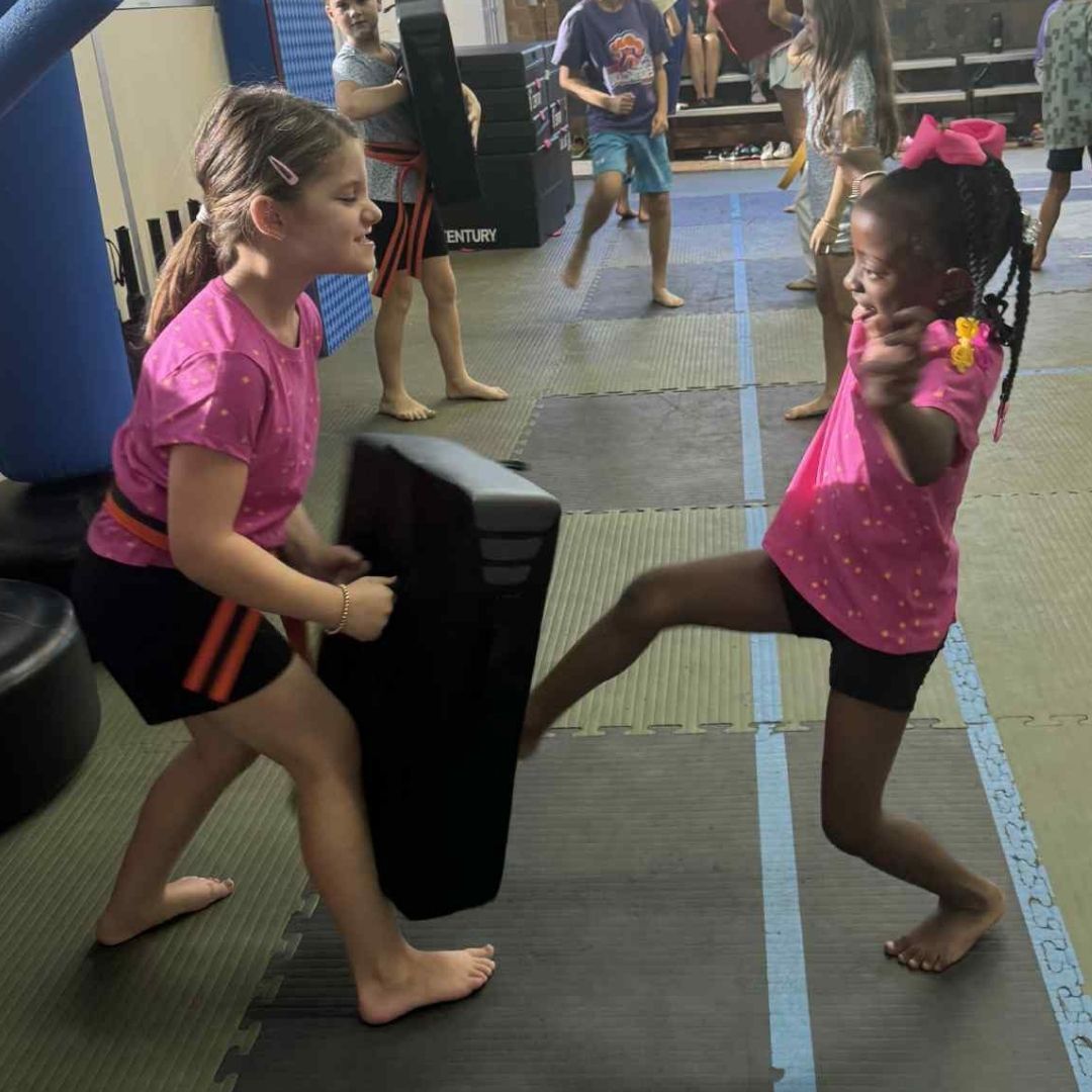 Two boys on a mat practicing Jiu-Jitsu. One boy is on top, giving a thumbs-up.