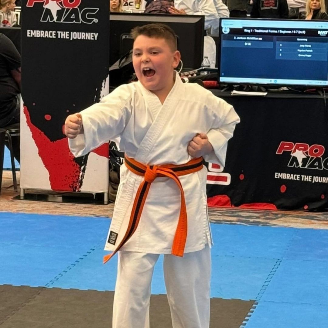 Two children practicing Brazilian Jiu-Jitsu on a mat. One child in white gi has the other in a leg lock. A girl watches.
