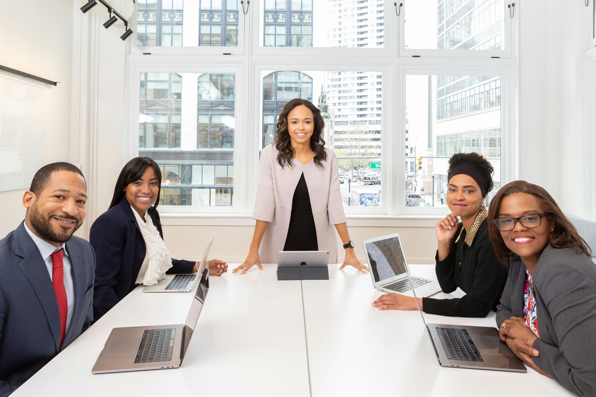 Business team gathered around a conference table with laptops, smiling in a well-lit room with city view.