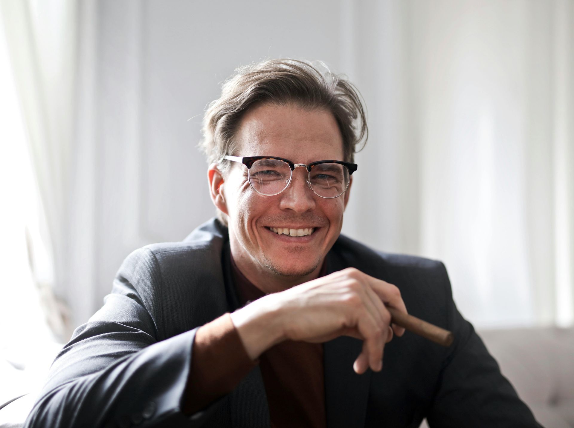 Man wearing glasses and suit, smiling, holding cigar.