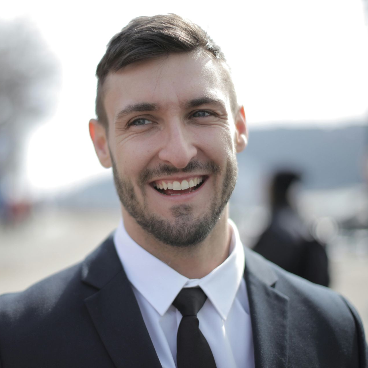 Man in a suit smiles broadly, looking off-camera.
