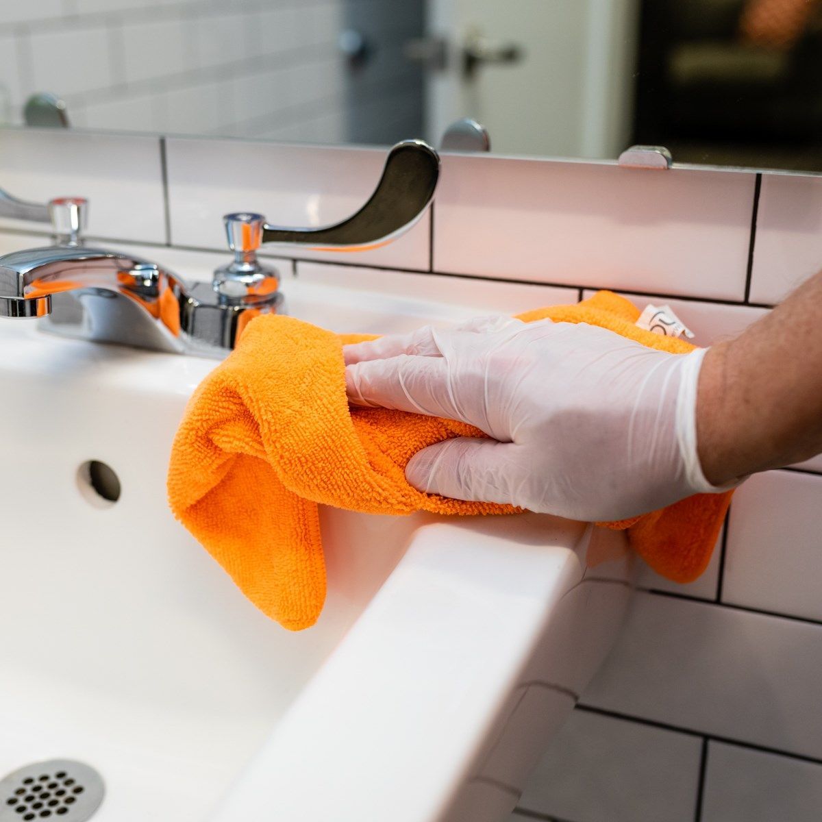 A person wearing gloves is cleaning a sink with an orange towel