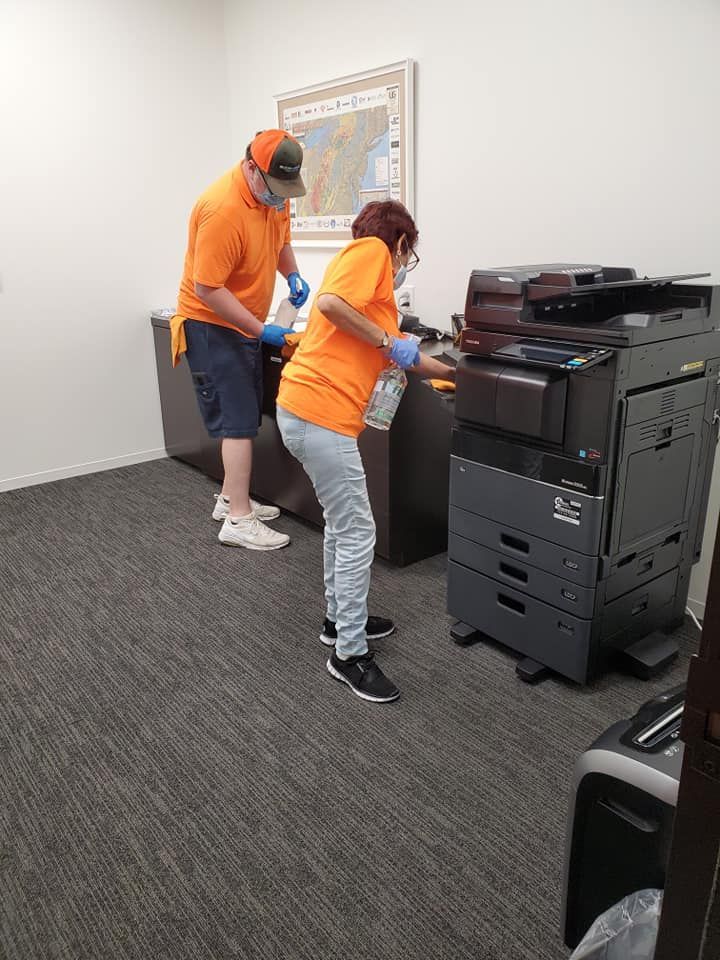 A man and a woman are cleaning a printer in an office.