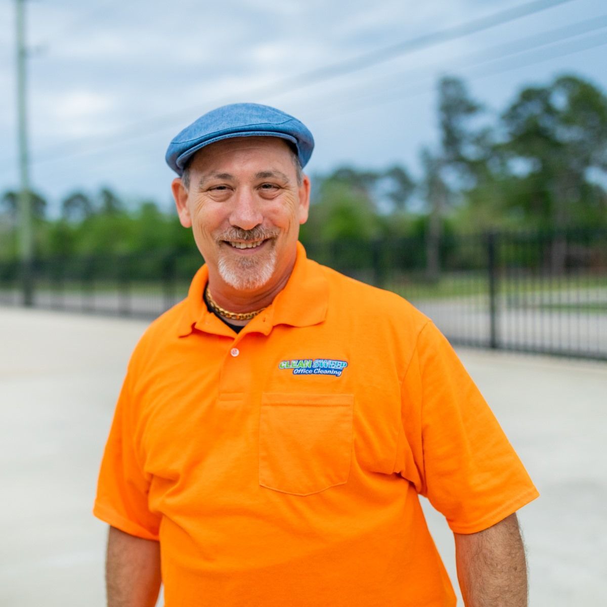 A man wearing an orange shirt and a blue hat smiles for the camera