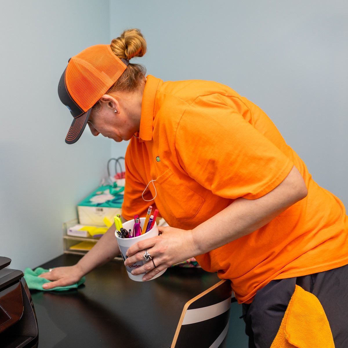A woman in an orange shirt is cleaning a desk
