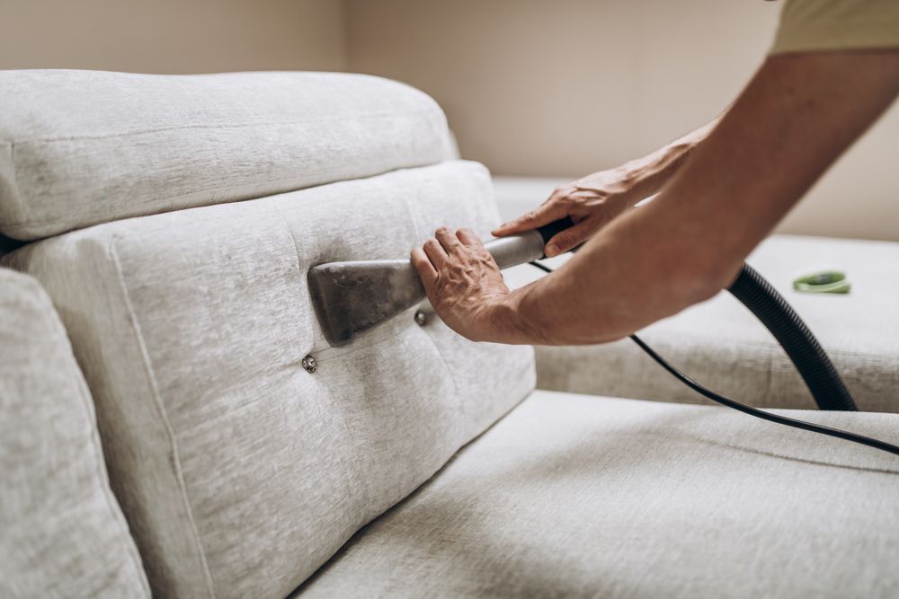 A person is cleaning a couch with a vacuum cleaner.