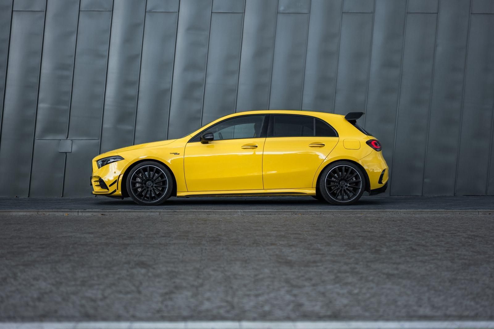 Una Mercedes-Benz Classe A hatchback gialla parcheggiata su una strada grigia accanto a un muro grigio.