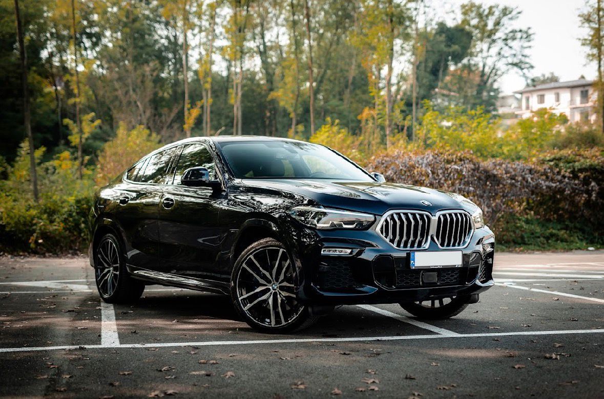 SUV BMW X6 nero parcheggiato in un parcheggio, alberi sullo sfondo, giornata di sole.