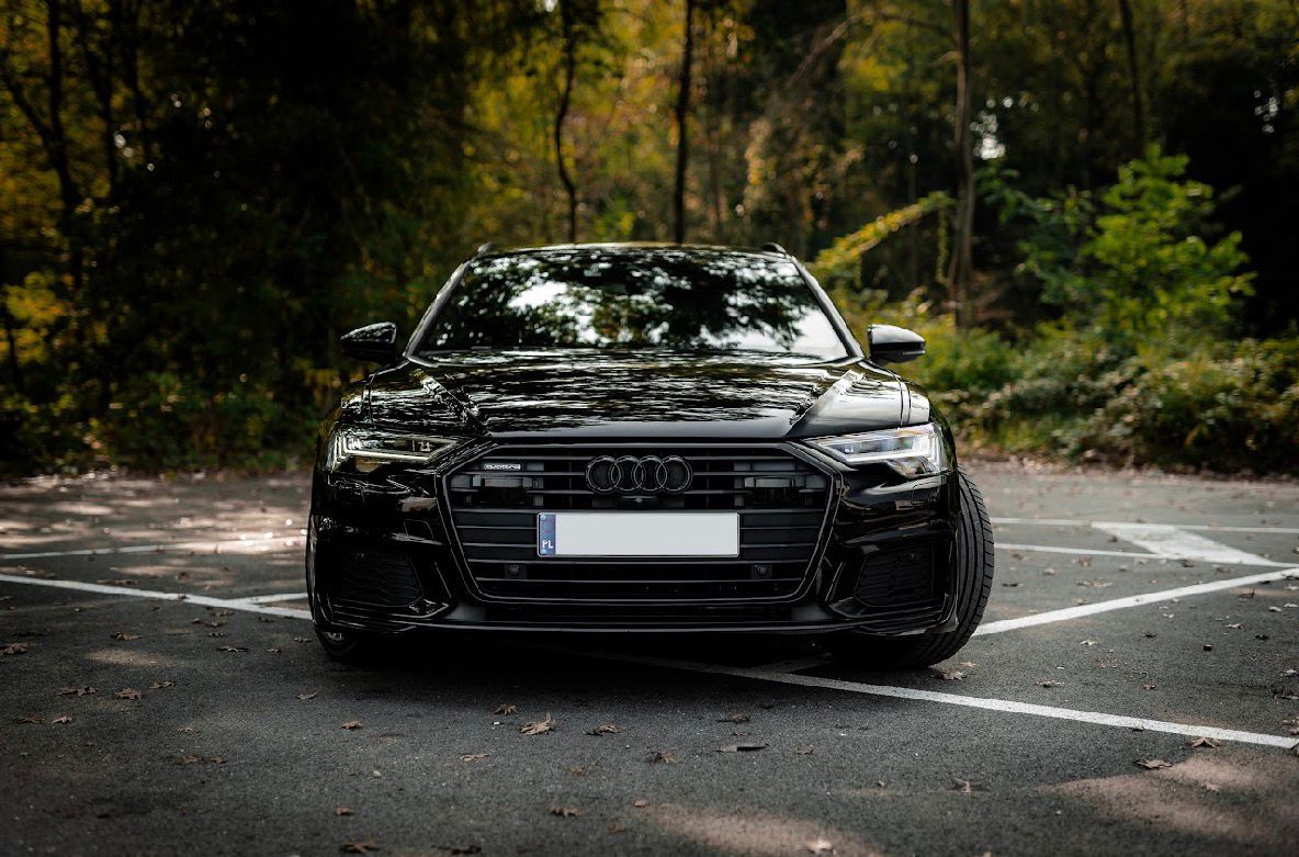 Audi nera parcheggiata sull'asfalto davanti agli alberi.