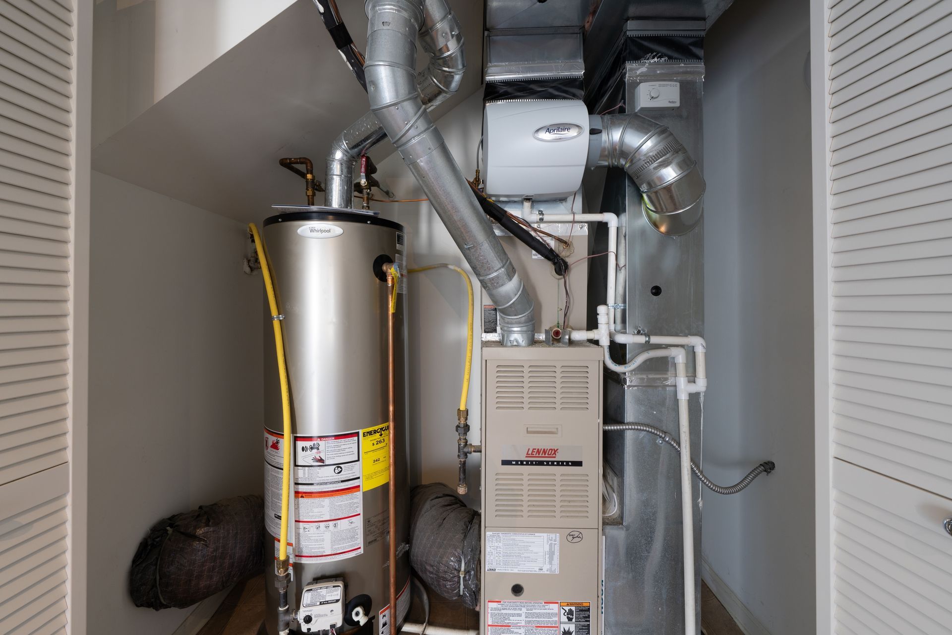 Utility closet with furnace, water heater, and exposed ducts and pipes