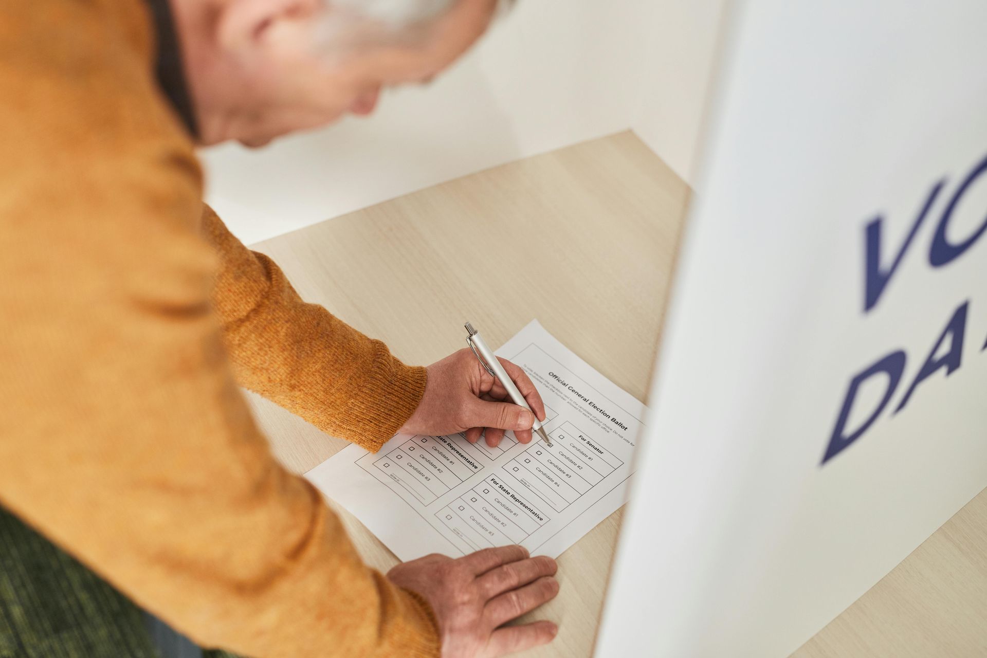 Man filling out a form at a polling station, writing with a pen on a white sheet.