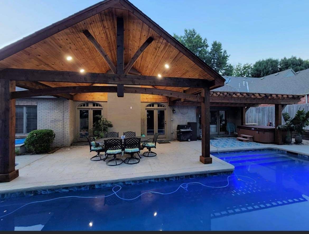 A large swimming pool with a table and chairs under a wooden pergola.