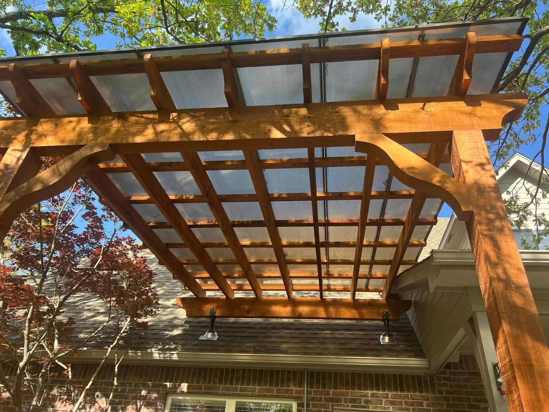 A wooden pergola with a clear roof is sitting on top of a brick house.
