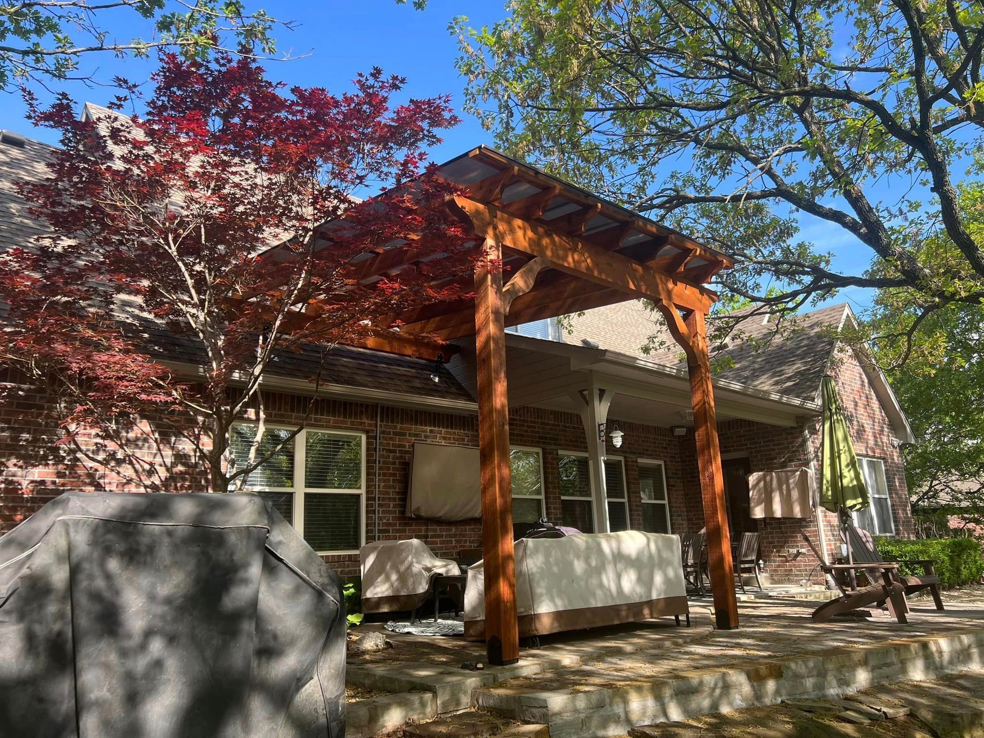 A wooden pergola is sitting on top of a patio in front of a brick house.