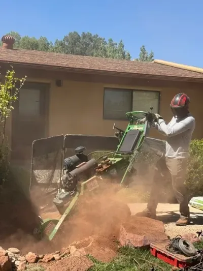 Person cutting a log with a chainsaw beside stacked firewood outdoors