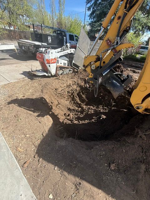 Yellow excavator digging soil beside a white skid steer on a sunny construction site