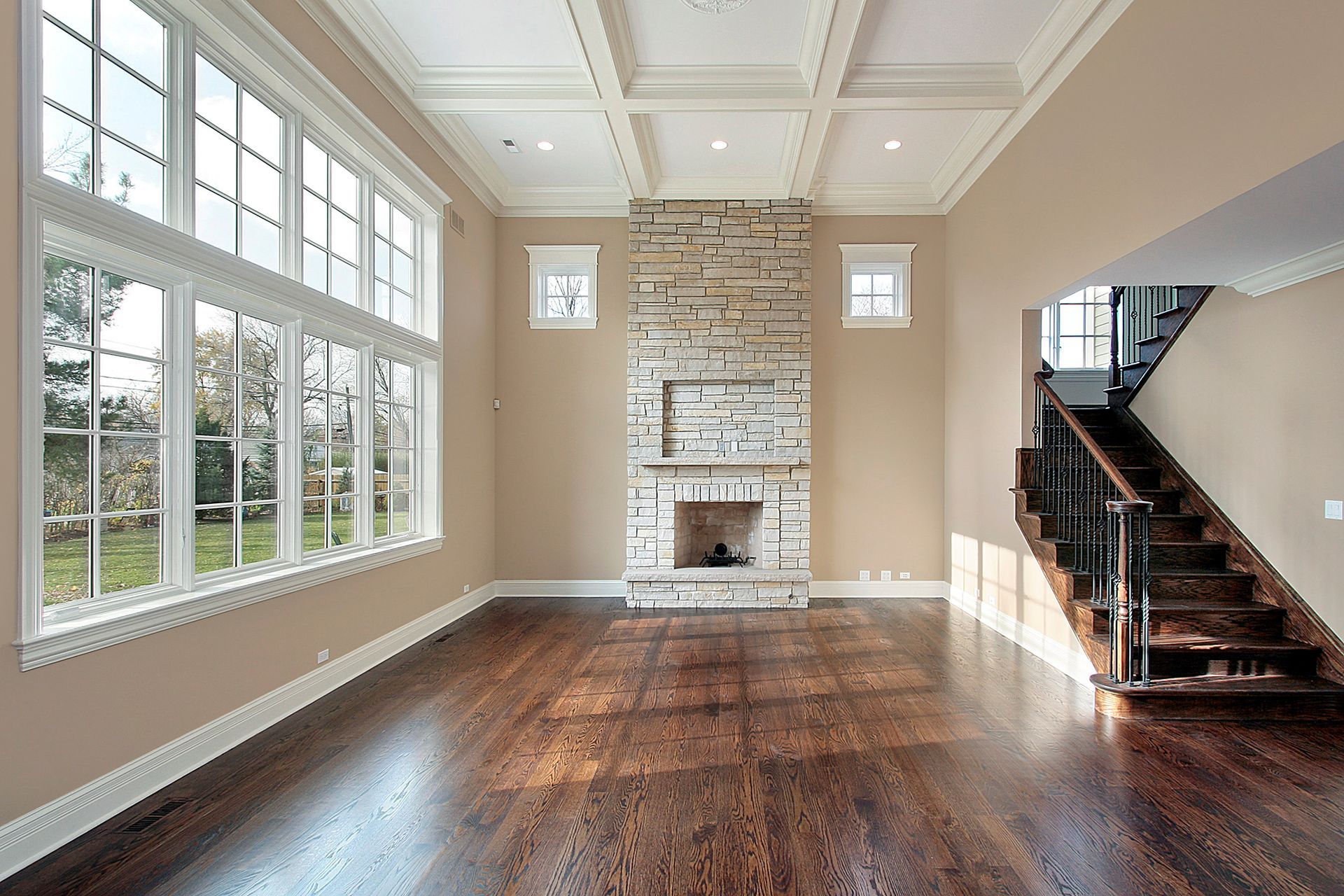 Empty living room with large windows, stone fireplace, and dark wood floors.
