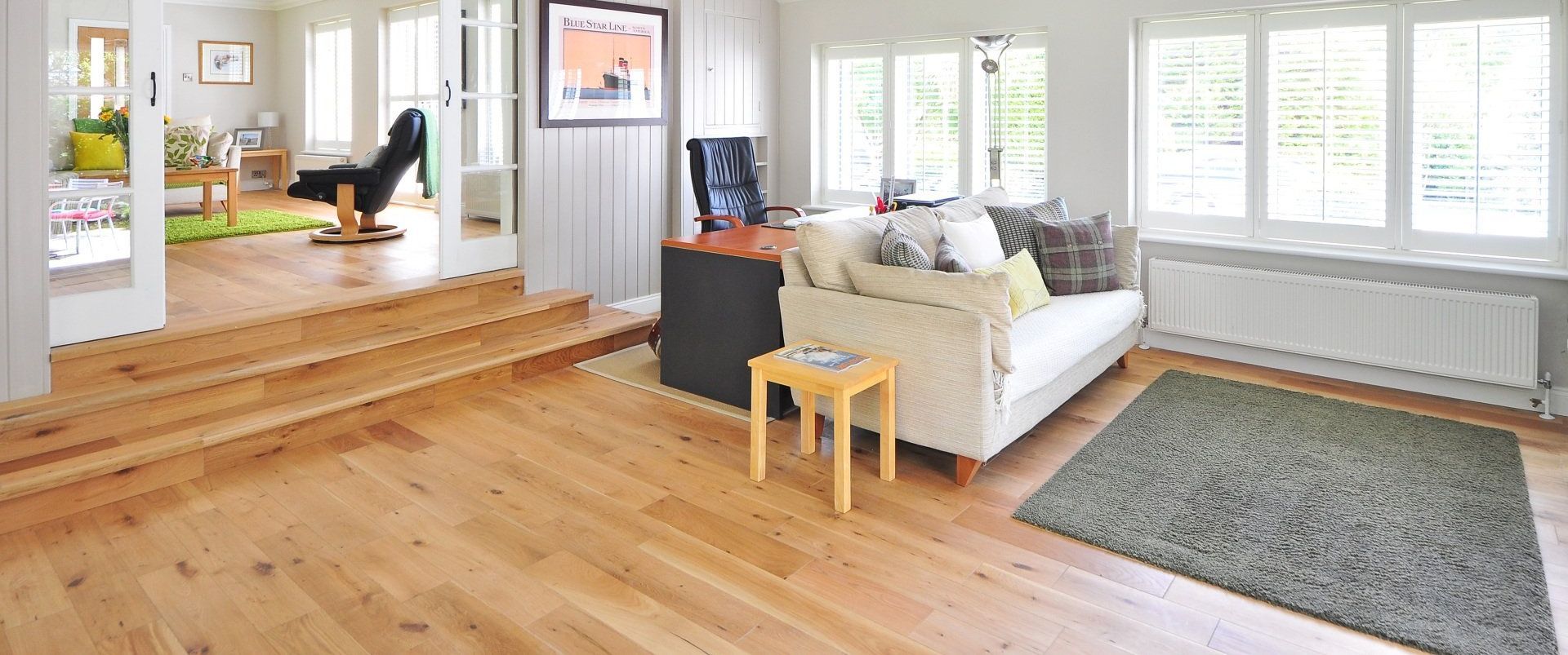Bright living room with hardwood floors, a white couch, rug, and large windows.