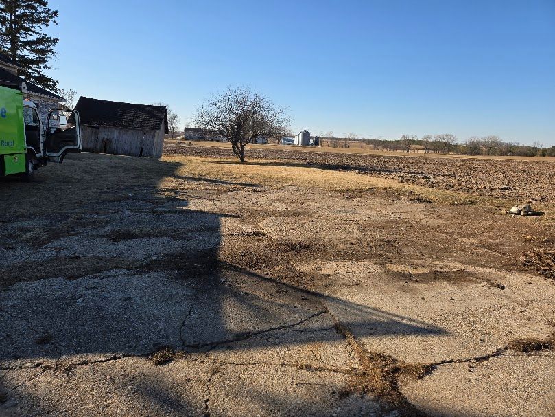 Cracked concrete foreground leads to a field, weathered barn, and blue sky.