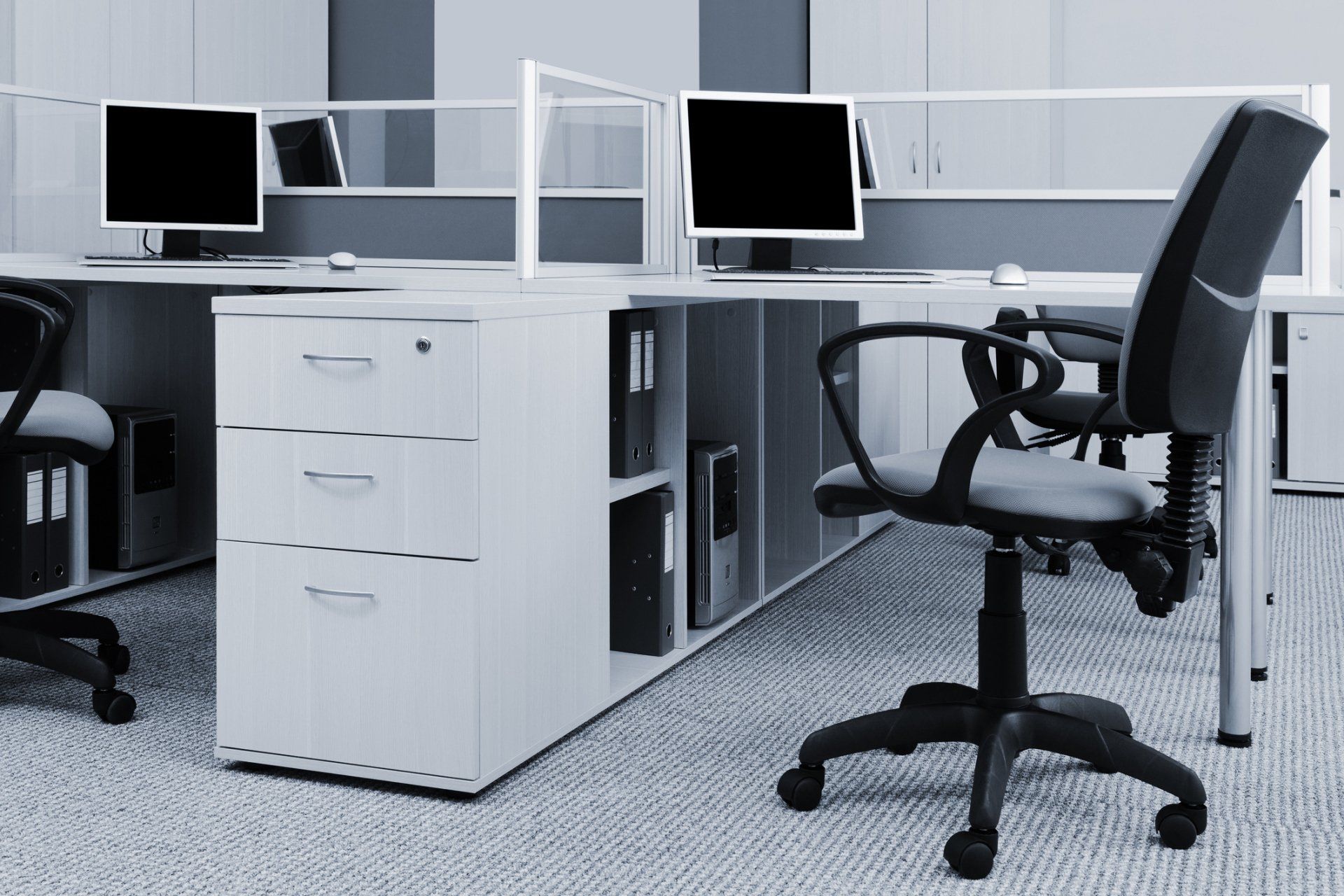 Modern office cubicle with computer monitors and black office chairs.