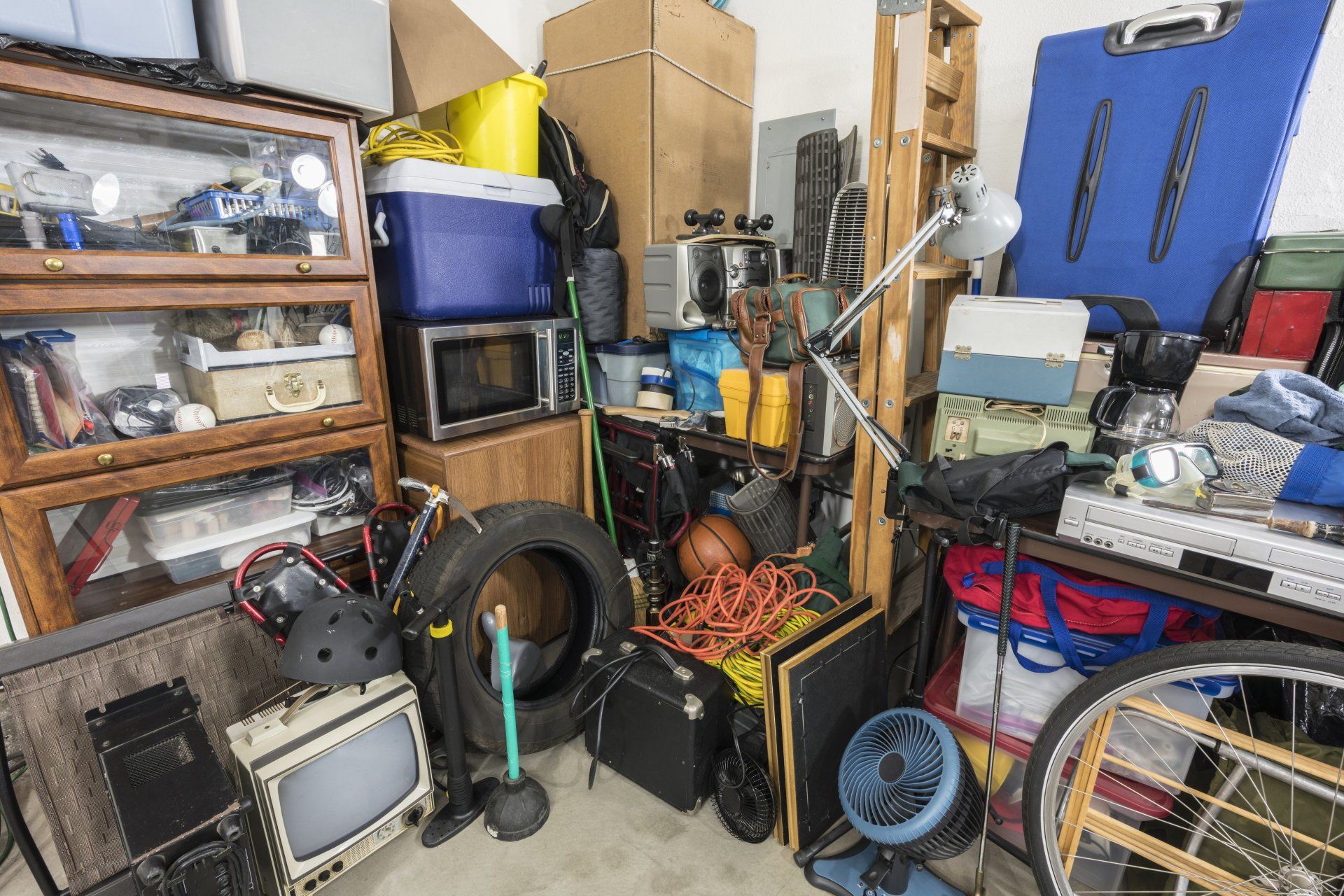Cluttered storage area with boxes, appliances, tires, and various items piled haphazardly.
