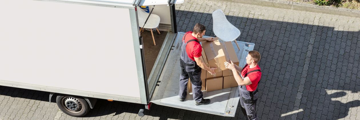 Two men loading furniture into a truck. One wears a red shirt with