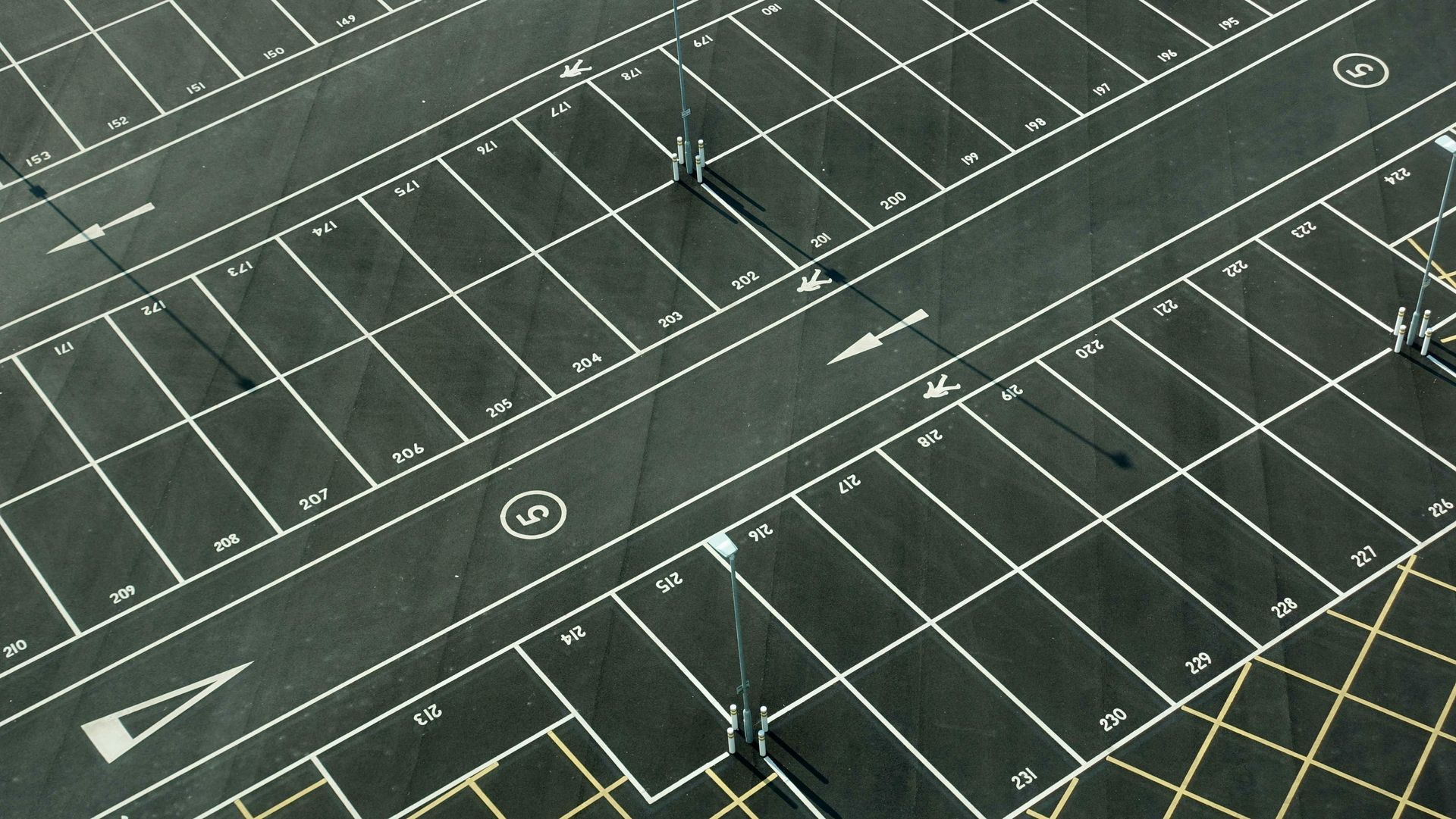 Aerial view of an asphalt parking lot with white painted parking space lines and arrows.