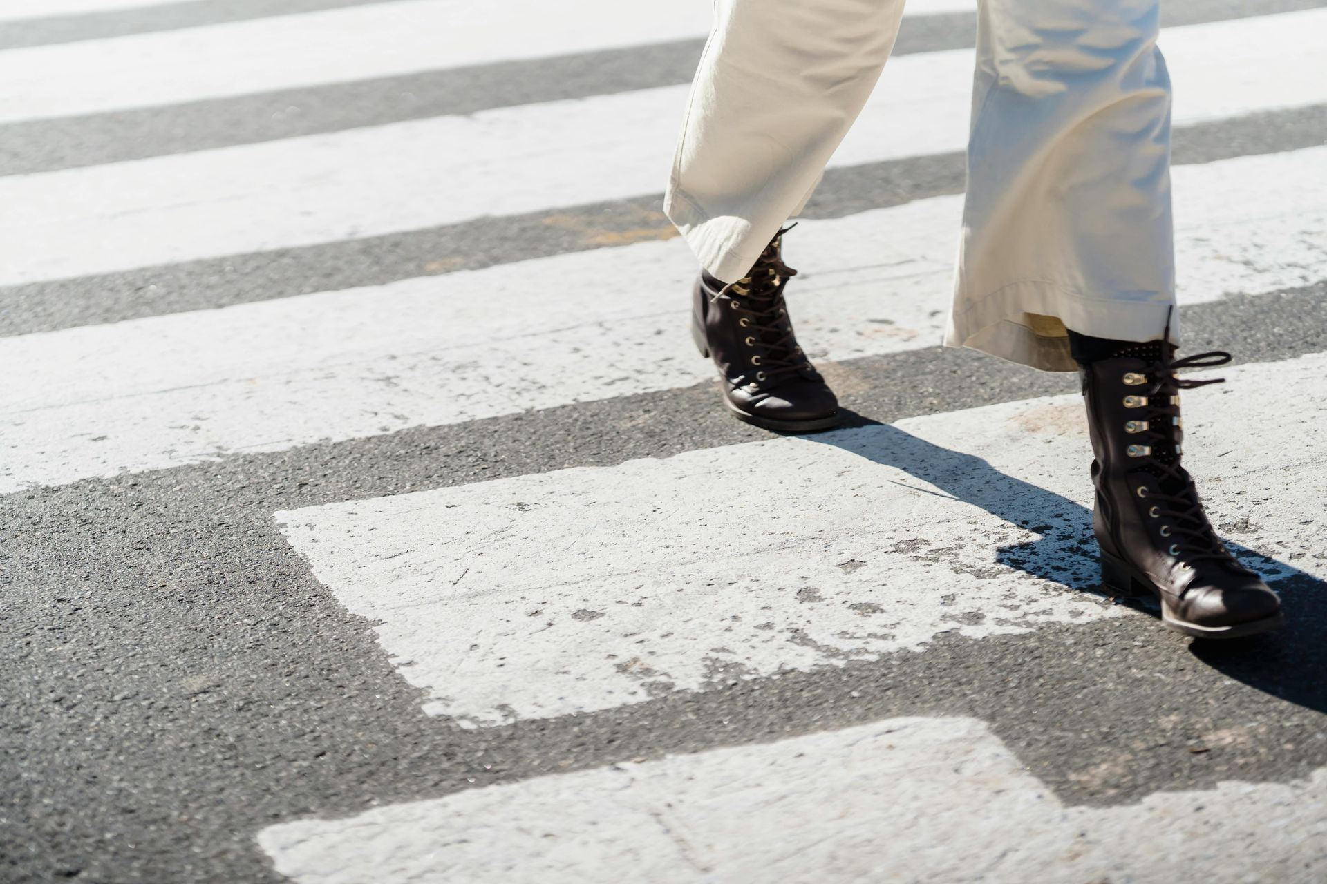 Person in cream pants and black boots walking across a crosswalk.