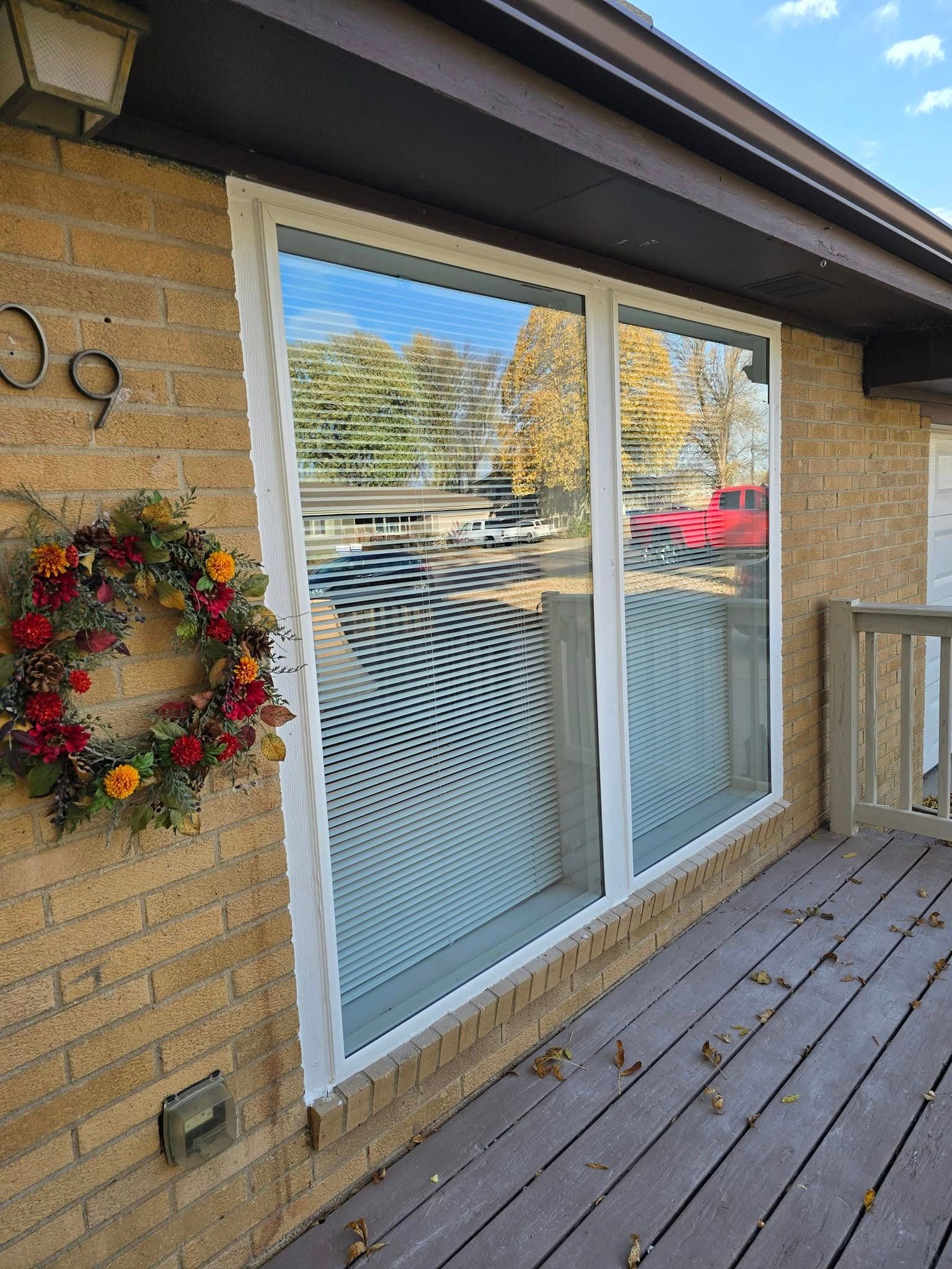 A wreath is hanging on the side of a brick house next to a window.