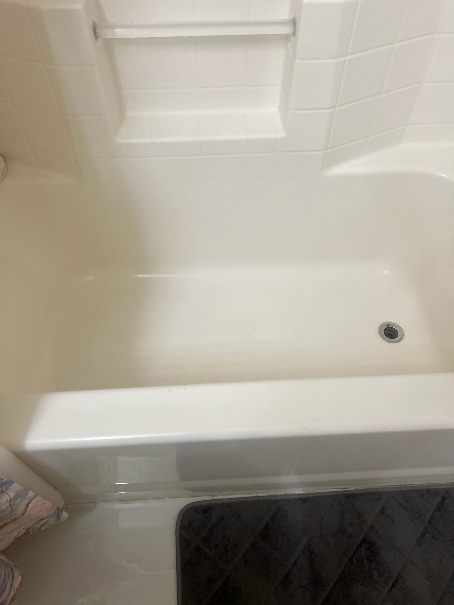 Cream-colored bathtub with a tiled ledge and dark gray bath mat.