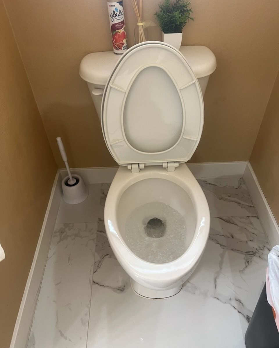 Toilet with the seat up in a small bathroom; the toilet bowl is clean, floor is marble tile.