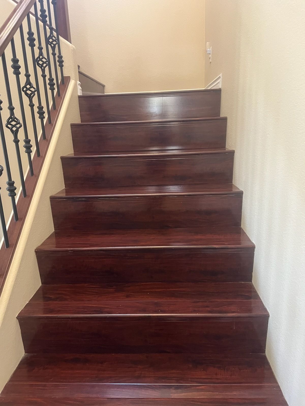 Wooden staircase leading upwards; mahogany-colored steps. Black wrought-iron railing on the left.