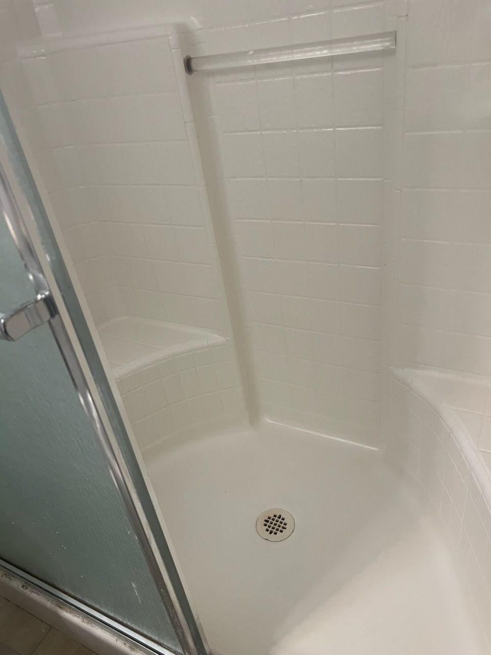 Corner shower with built-in seat, white walls, and a glass door.