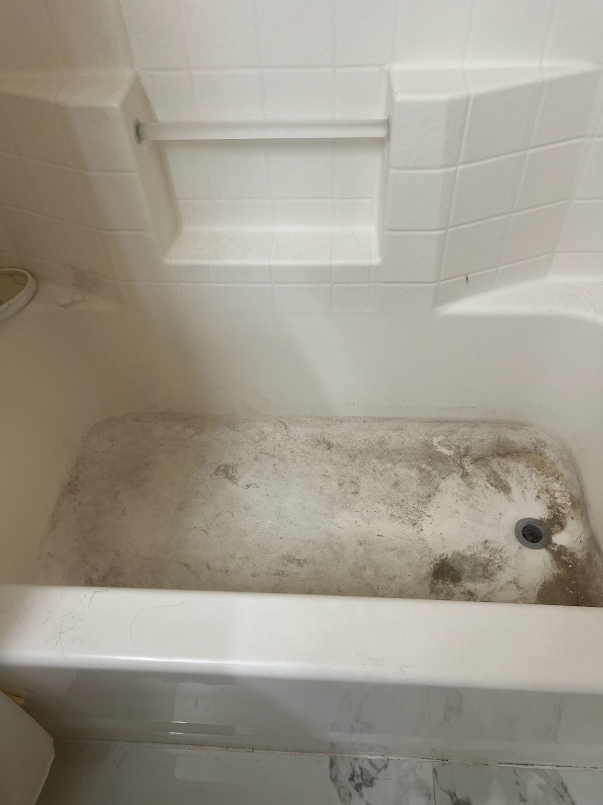 A dirty bathtub with soap residue and grime buildup. White walls surround it.