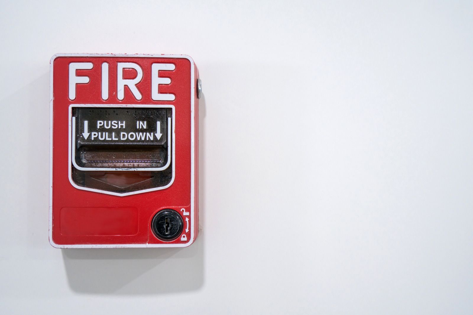 A red fire alarm is hanging on a white wall.